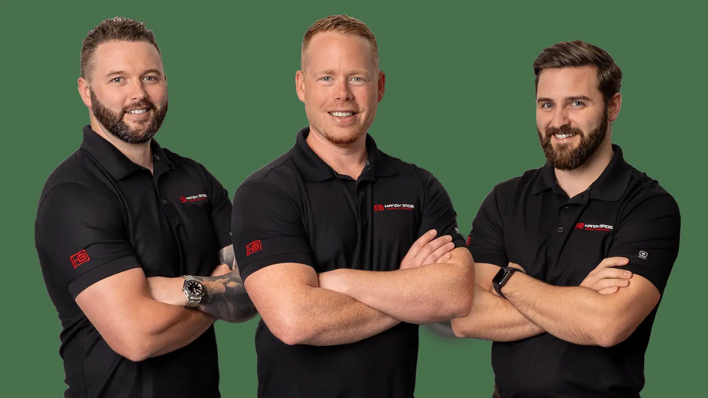 Three men in black polo shirts with a logo cross their arms and smile at the camera against a green background, posing as a team.