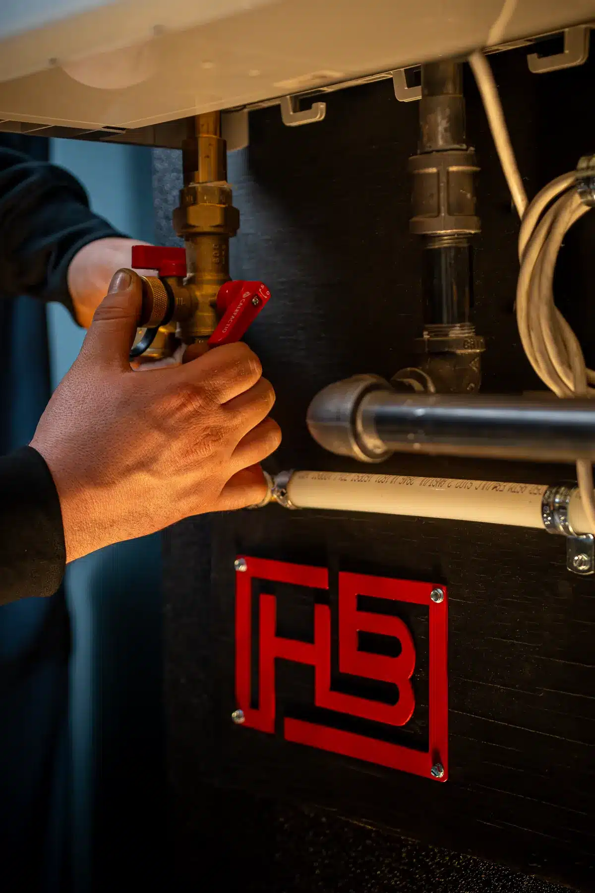 Close-up of a technician turning a red lever valve on a copper pipe under an industrial cabinet.