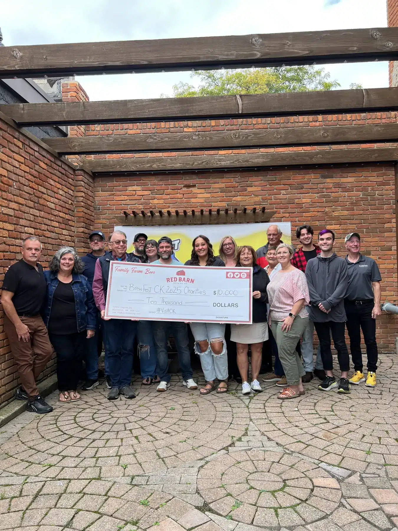 Group of people posing in a brick courtyard, holding a large ceremonial check for ,000 from Red Barn Brewing.