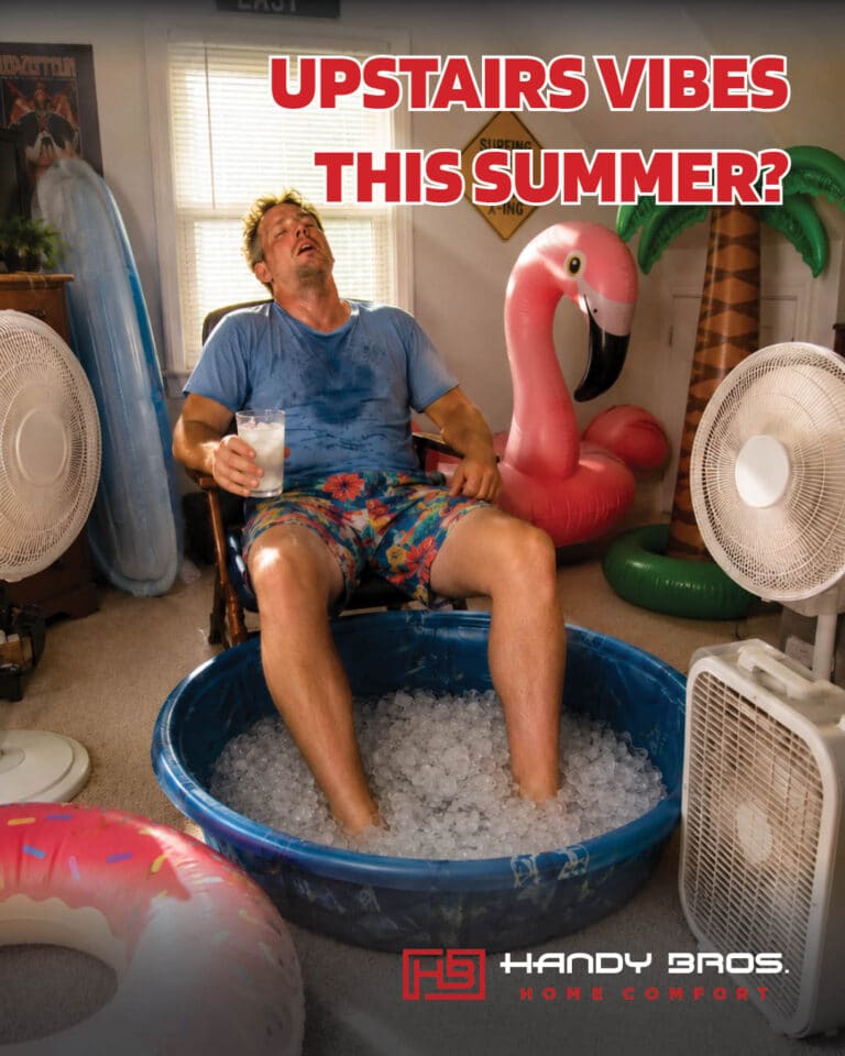 Man lounging in a blue ice-filled tub, holding a drink, in a room crowded with pool inflatables and fans nearby.